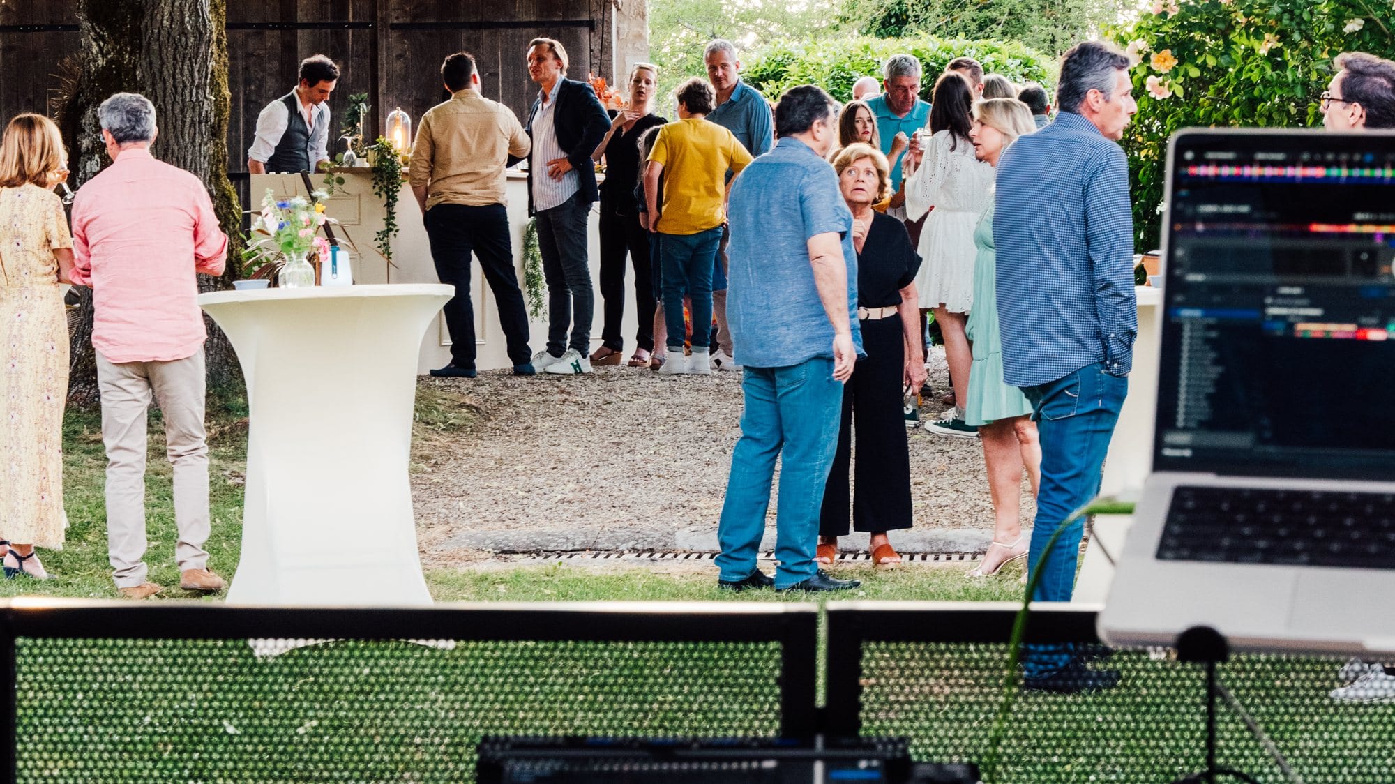 Des invités discutent un verre à la main, sous une tente, lors d’une soirée privée en extérieur.