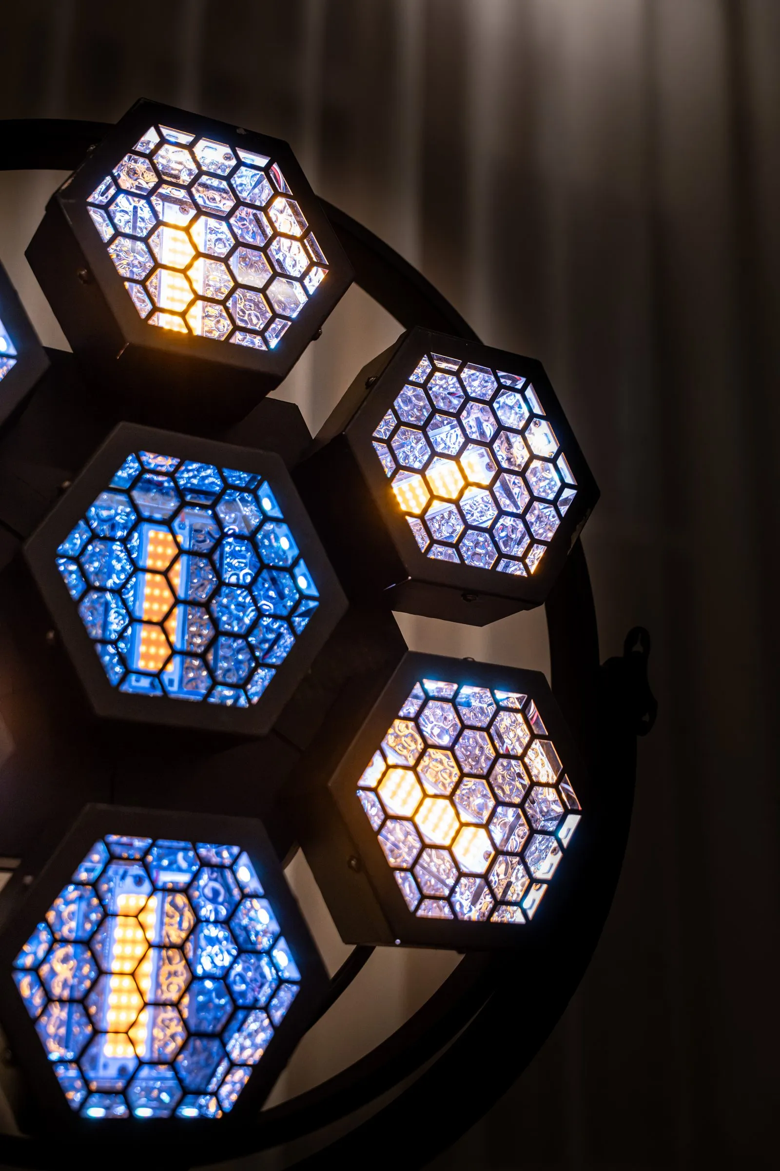 Détail de côté d’un projecteur : lentilles alvéolées éclairées de bleu et d’ambre dans leur cadre noir.