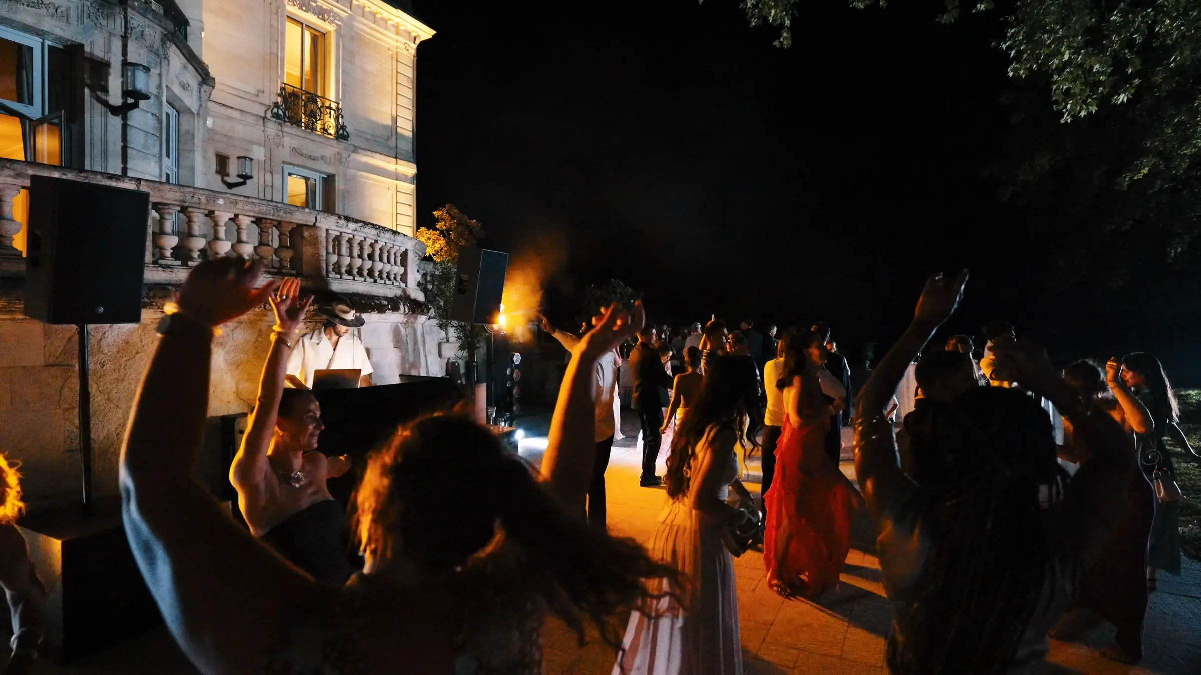 Invités qui dansent les bras en l’air, le DJ derrière sa console, de nuit.