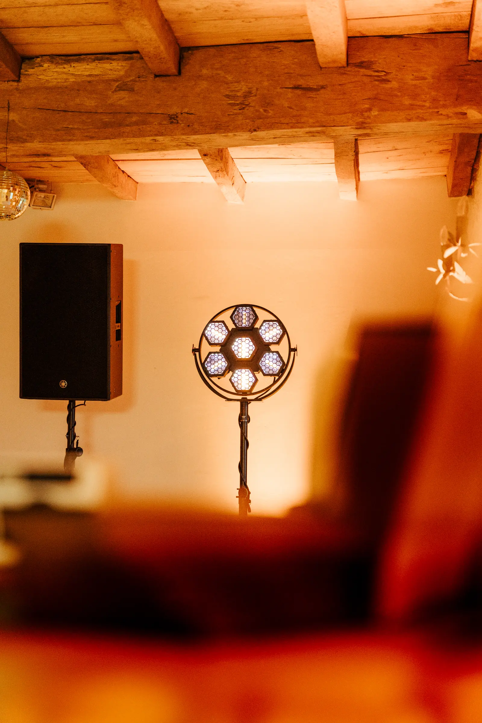 Enceinte et projecteur lumineux dans une grange en pierre aux poutres apparentes, éclairage chaud et tamisé.