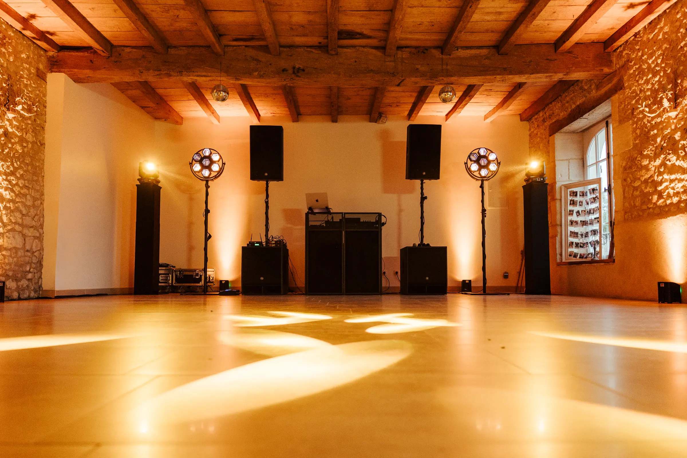 Vue d’ensemble d’une salle de réception en pierre, console DJ, enceintes et projecteurs de chaque côté, piste de danse éclairée.