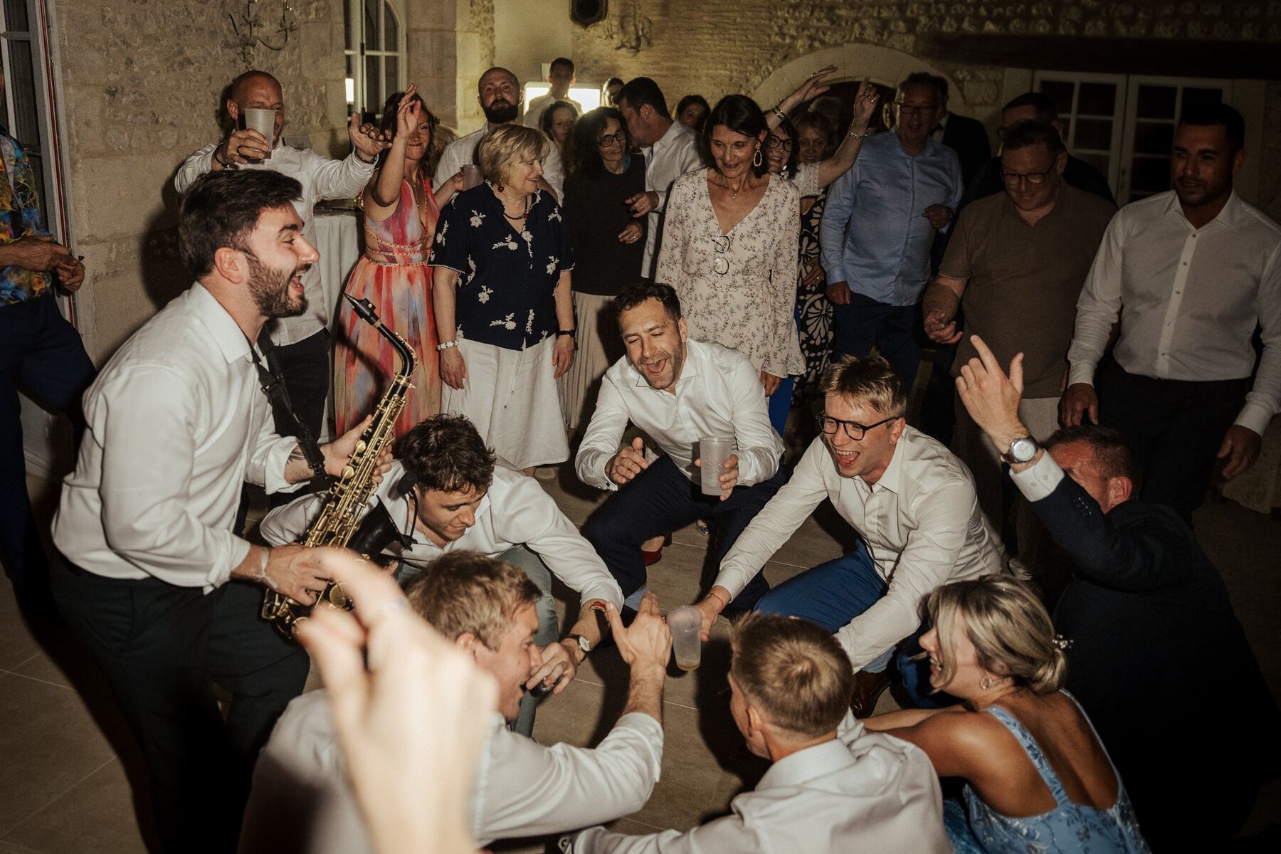 A saxophonist playing among the guests, mid wedding party in a stone-walled hall.