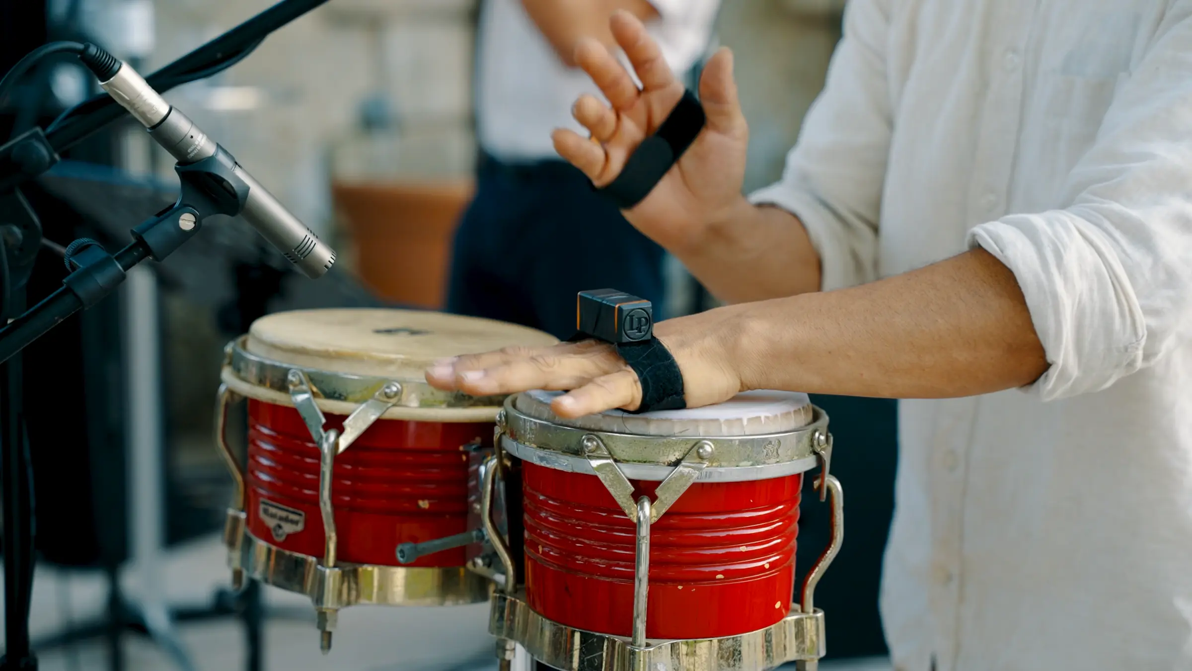 Mains d’un percussionniste sur des bongos rouges.