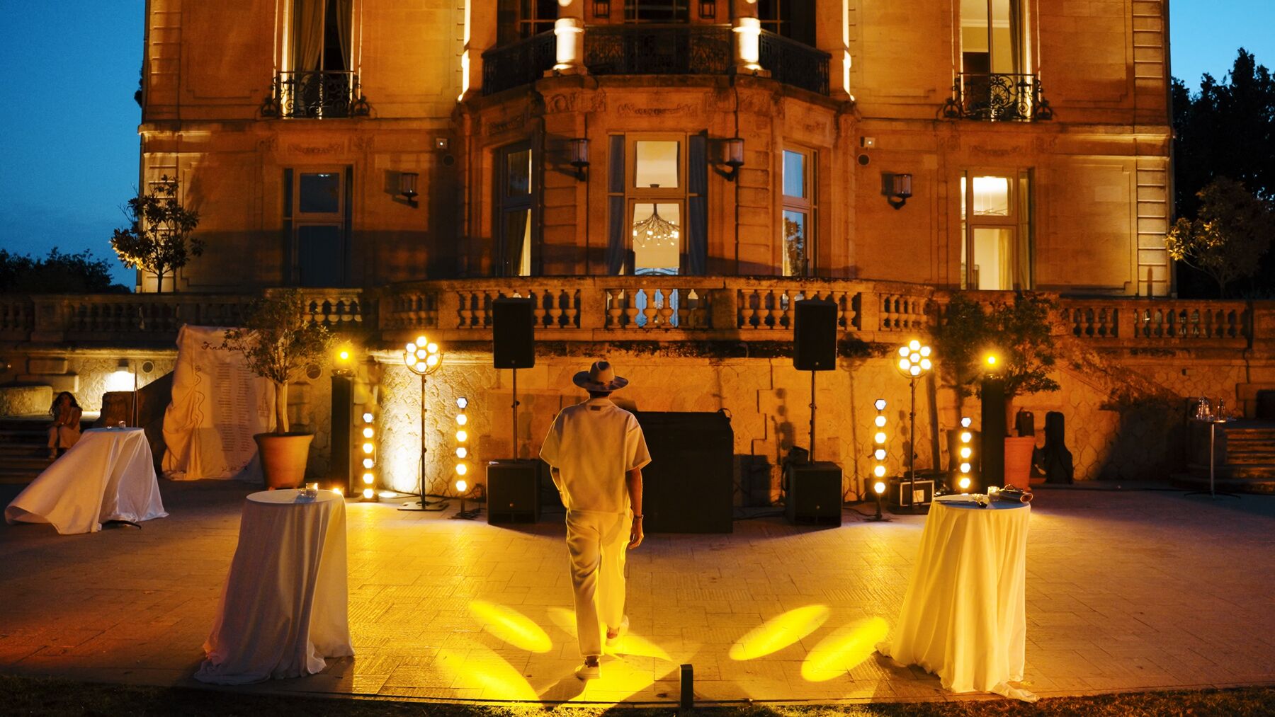 A château façade lit up at night, with the DJ setup and decorative lighting on the terrace.