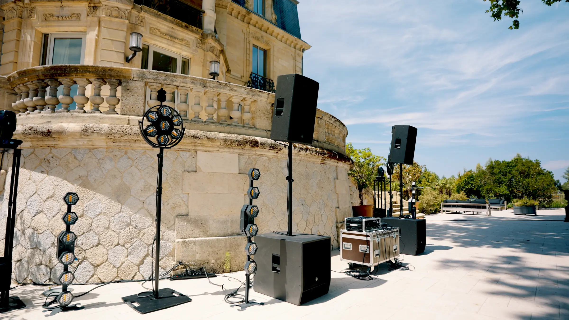 Enceintes, caissons de basse et projecteurs sur la terrasse d’un château, en plein jour.